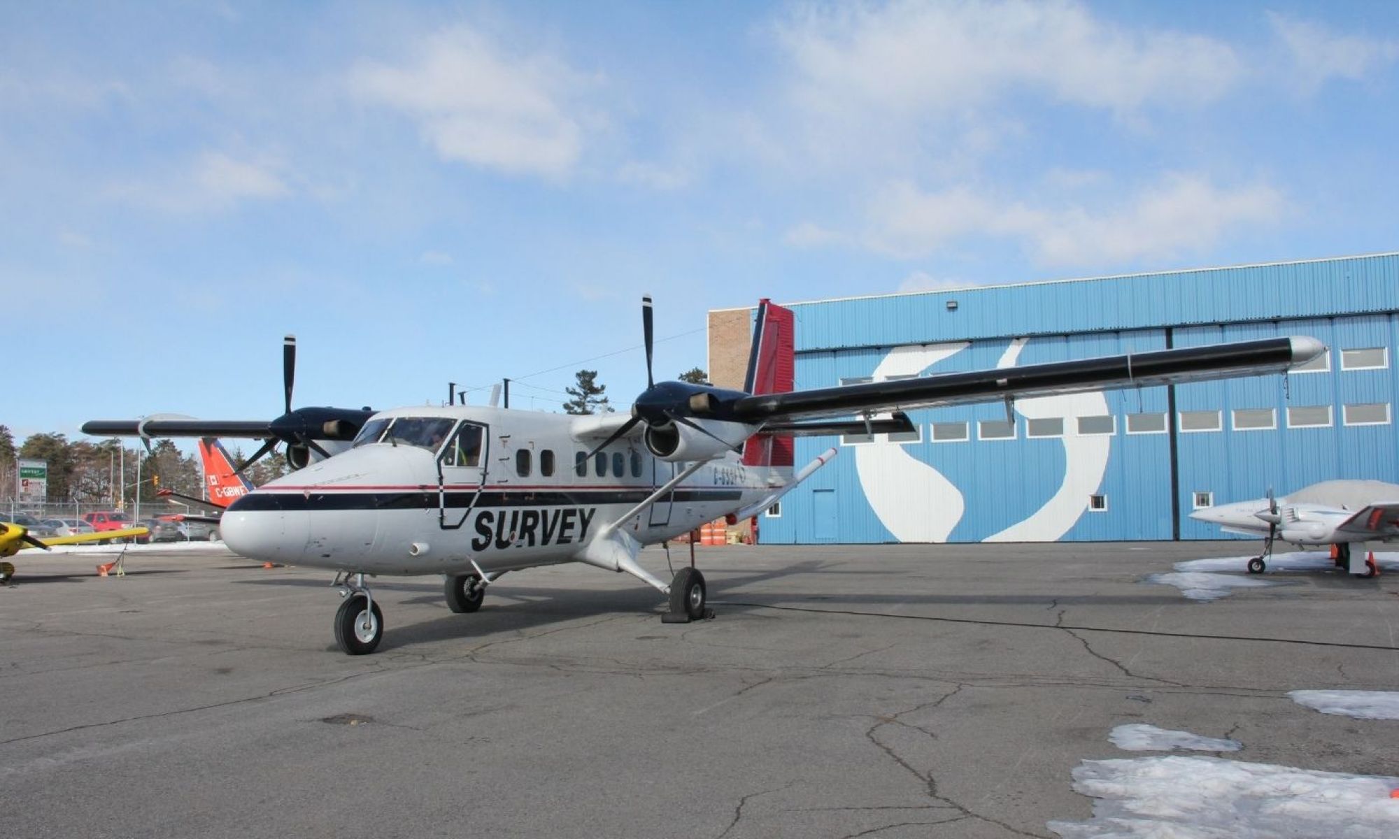 A twin engine plane with the word 'survey' written down its side in front of an aircraft hangar.