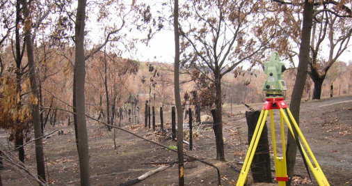 Photo of burnt trees and fences with surveying equipment in the foreground.  