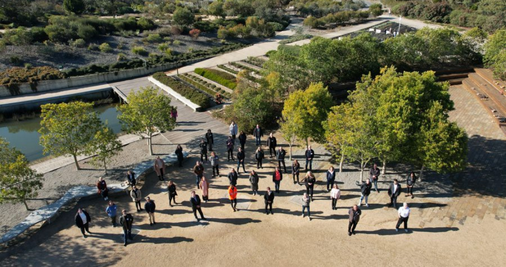 An aerial photograph of workshop participants with green gardens behind them.  